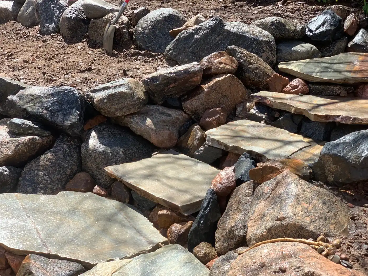 Flagstone steps in stone wall Flagstone paver steps set into a natural stone retaining wall with rock beds in Parker, CO