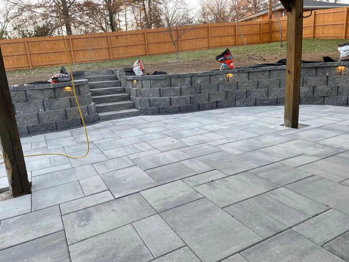 Paver patio and pergola build Large gray paver patio with pergola posts and a block retaining wall under construction in Parker, CO